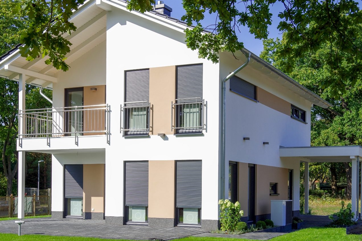 Modernes zweistöckiges Wohnhaus mit Balkon und großen Fenstern, umgeben von Bäumen.
